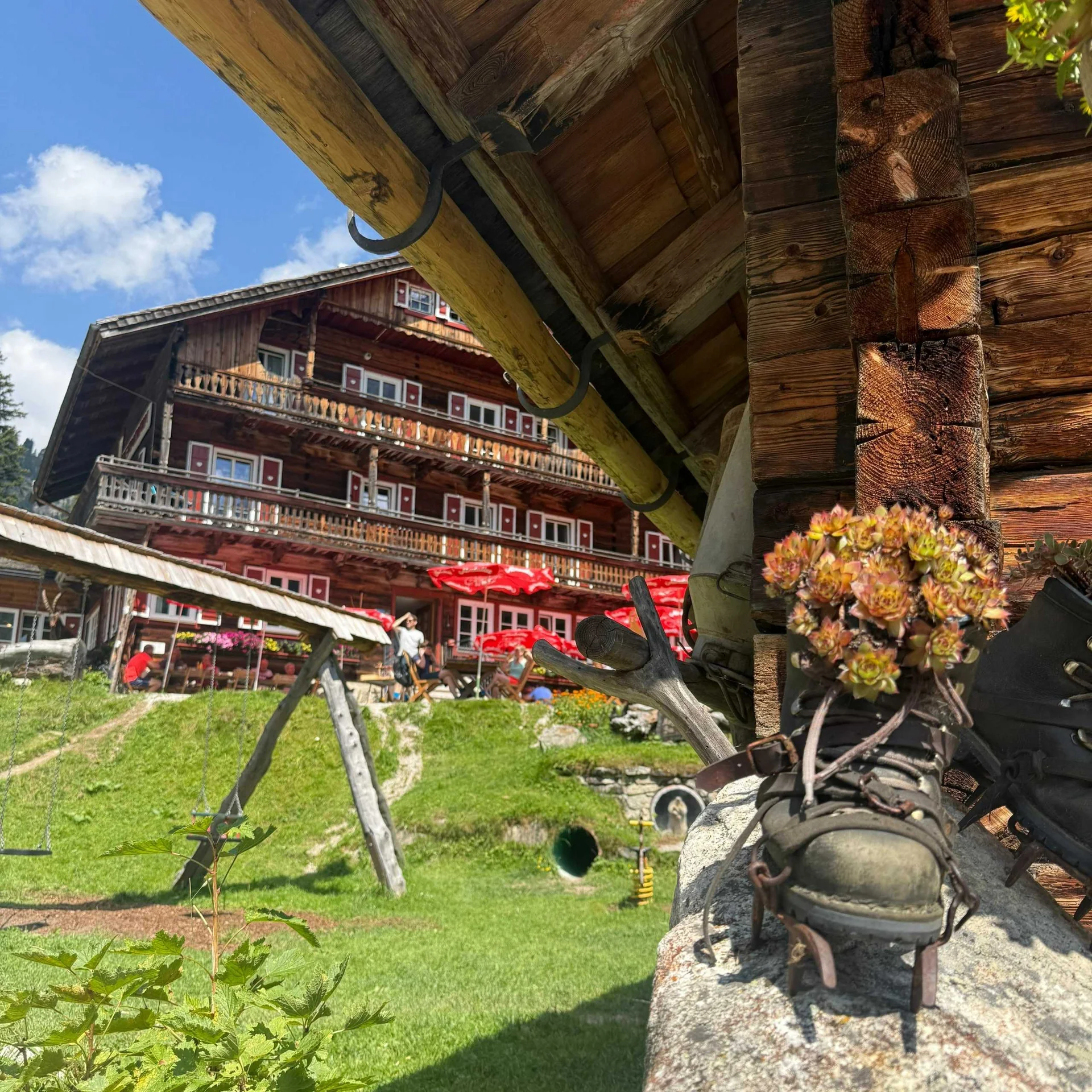 Altes Holzhaus mit Blumenschuhen und rotem Sonnenschirm im Garten