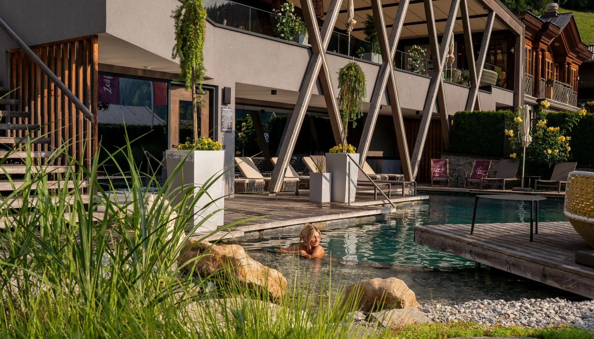 Frau entspannt im Außenpool eines modernen Hotels mit Holzterrasse und Pflanzen