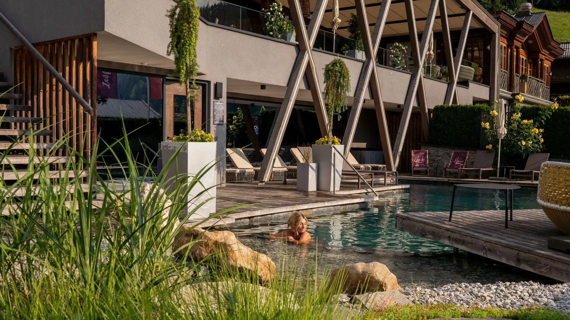 Wellness Woman relaxing in outdoor pool at modern hotel with wooden deck and greenery