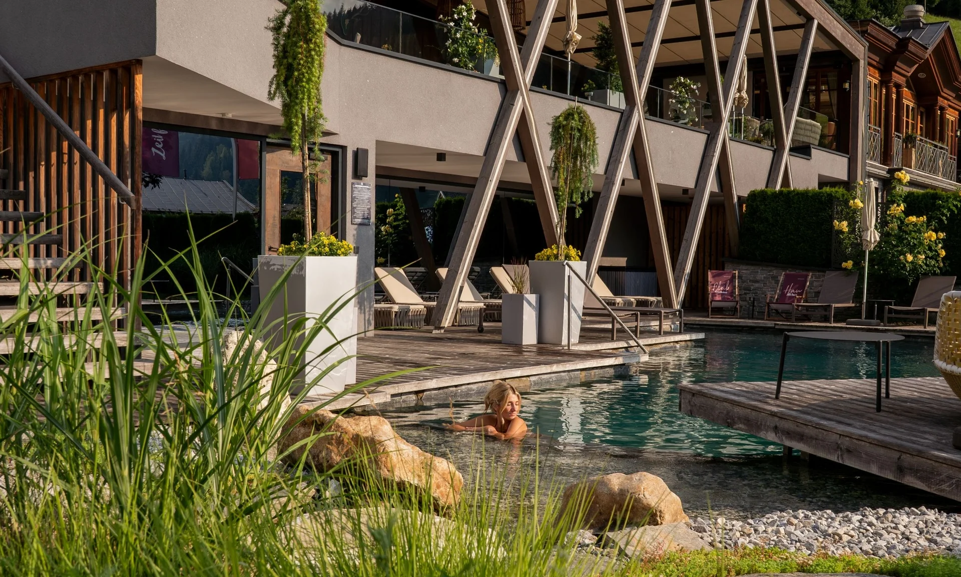 Frau entspannt im Außenpool eines modernen Hotels mit Holzterrasse und Pflanzen