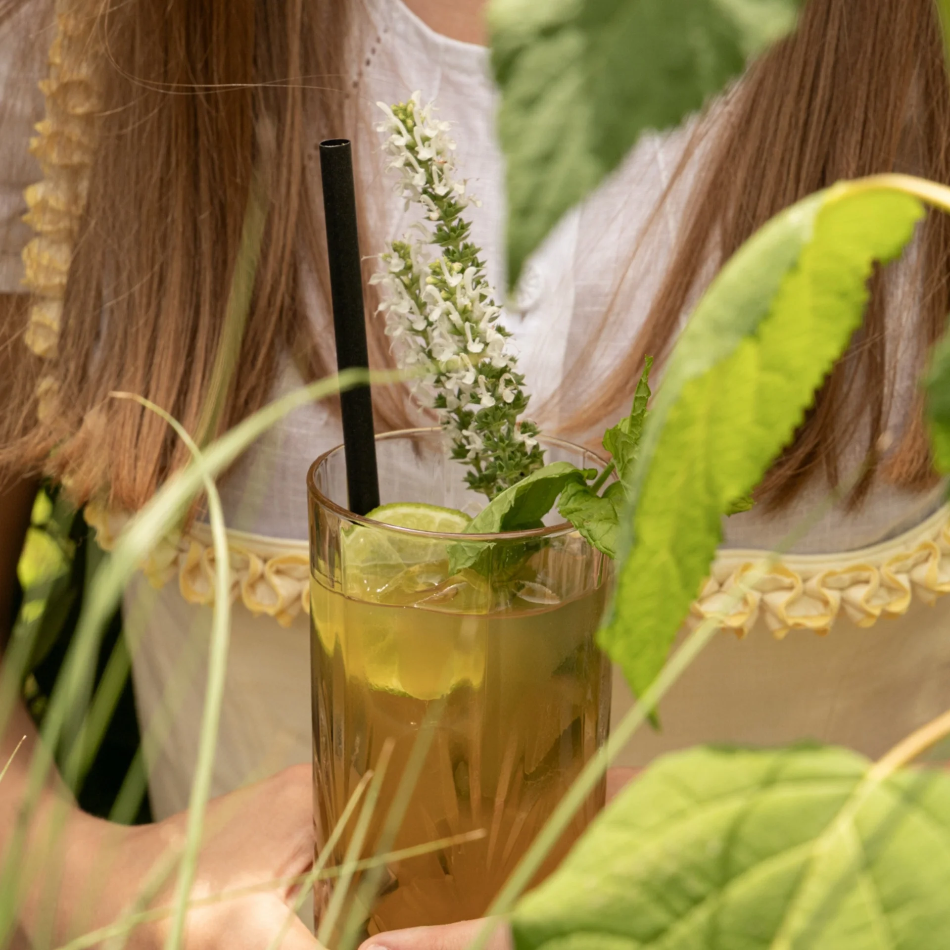 Colour Hunting Sommerchallenge Glas mit Minztee, Limettenscheiben und frischer Blüte, gehalten von Person