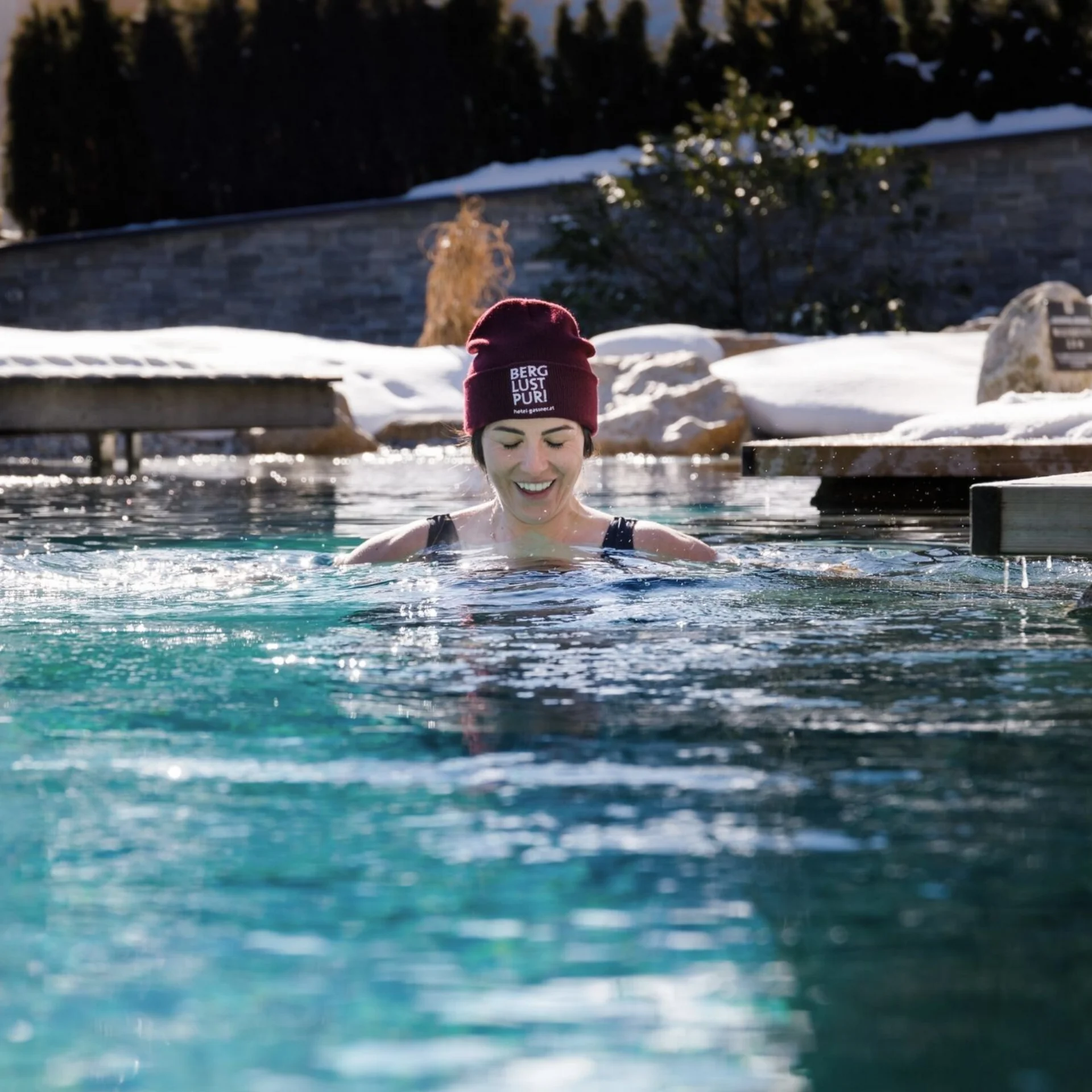 Saunawelt Frau im Winter draußen im Pool mit Mütze und Schnee im Hintergrund