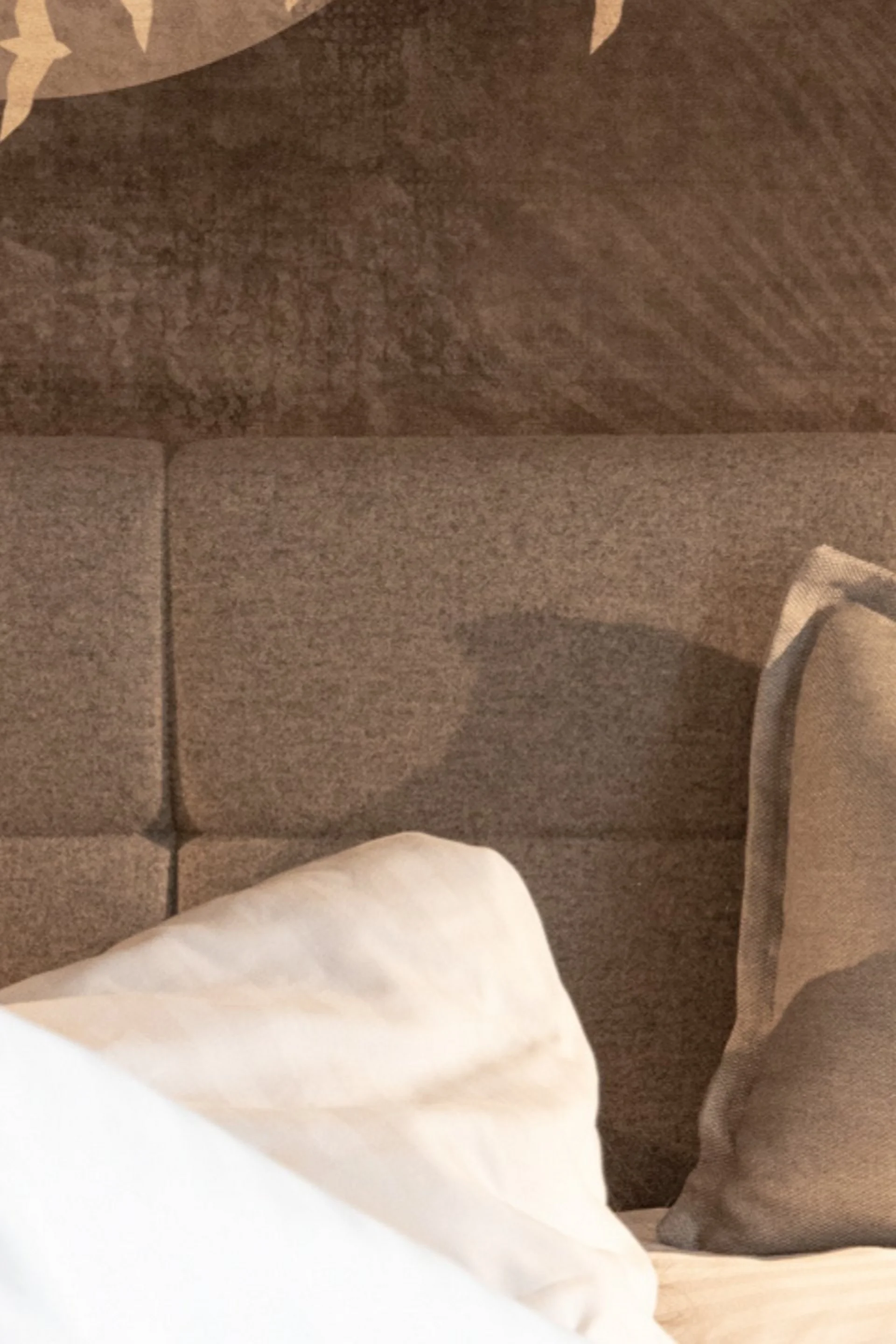 Person hebt ein Sektglas im Bett mit Kissen auf braunem Kopfteil