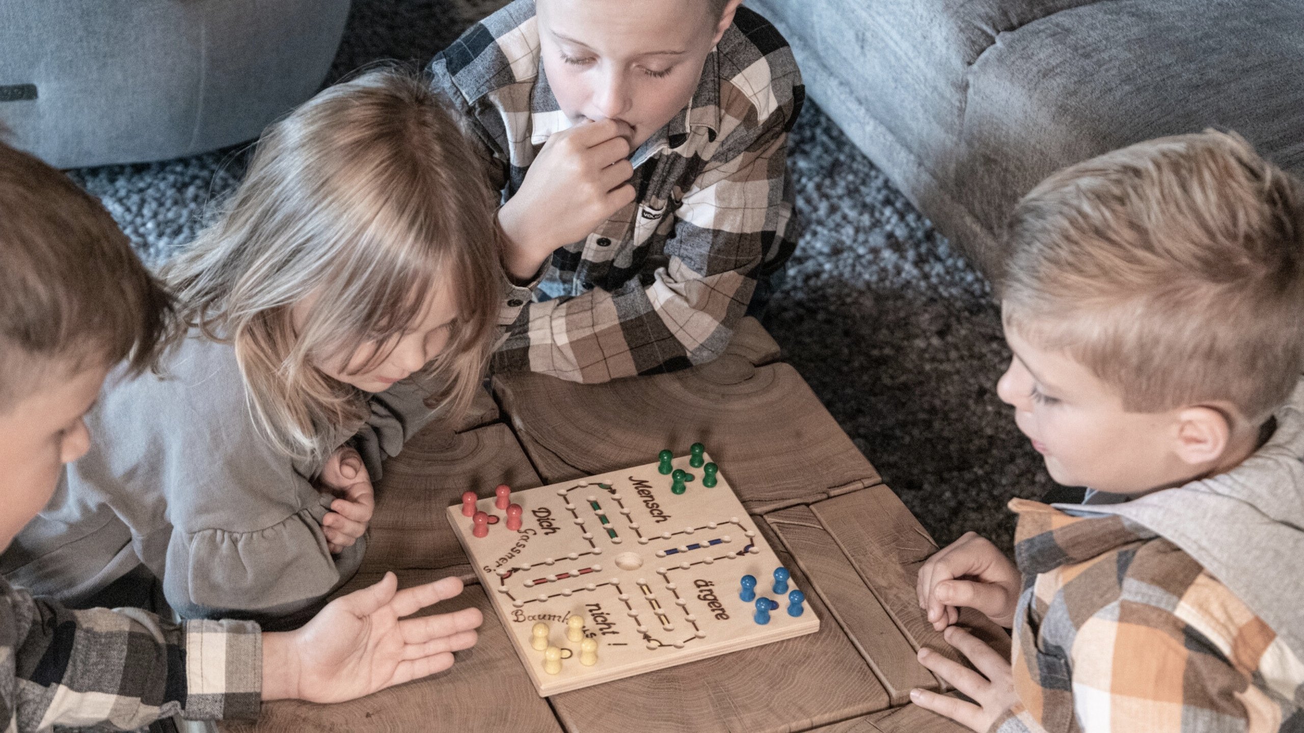Four children playing Ludo on a wooden table